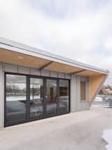 The mezzanine has rooftop access through large, south-oriented glazed doors. A steel awning offers shade to the mezzanine level during summer months, and the inside face is clad with plywood to visually extend the interior space outward.