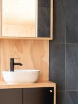 The plumbing fixtures and the dark ceramic tile reflect the black color of the cabinets. Round recessed handles are visually refined yet allow the panels on the vanity unit to be easily opened.