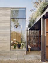 The entrance is through an enclosed courtyard, which features ipe (Brazilian walnut) timber fencing with an exposed painted steel structure topped with planters. The living room is visible through a glazed corner. 