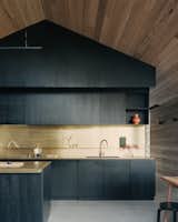 The kitchen is located in a bespoke timber joinery unit that divides the “living shed.” The timber has been stained black to contrast with the surrounding timber cladding, and brass counters and backsplashes echo the use of brass details throughout the interior. “Brass was a very special material—used sparingly—that has come to be a hallmark of the project,” says architect Ben Shields. 