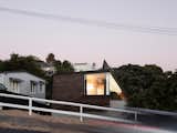 The house fronts the street with the large top story and a sharply angled roof that defines the staircase, creating a striking form—especially at night, when it is lit up from within.