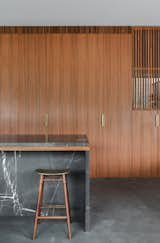 The spotted gum joinery in the kitchen dissolves into the sliding screen that divides the library/study from the living area. Brass details, such as the handles and the seat of the stool, add warmth to the material palette.