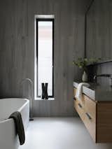 The use of raw, natural materials continues into the bathrooms, which feature timber joinery with concrete countertops that appear to float weightlessly.