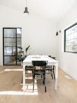 The main dining area in The House features a simple white dining table surrounded by black-painted chairs. The generous windows flood the space with natural light.