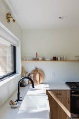 The shelves in the kitchen are crafted from pine and suspended using leather straps. These shelves display glasses, mugs, and a few select bowls, while everything else is neatly tucked away inside the cabinets, keeping the counters clear and drawing the eyes upward to the large horizontal window.  