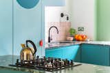 The kitchen backsplash features pink square Domus tiles framed by turquoise blue Mapei grout. The blue grout echoes the tones of the pale blue pantry and the teal cabinetry.