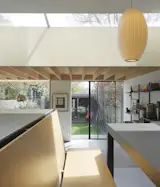 The sliding door is a slim-frame aluminium piece finished in matt black. Outside, the patio is finished with a light grey porcelain stone for ease of maintenance. In the dining area, two classic George Nelson pendant lights illuminate the working zones of the kitchen prep spaces.