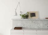 The Carrara marble forms the kitchen benchtop, a backsplash, and a small shelf for displaying personal items; while adjustable wall lighting allows the space to be configured for different tasks.