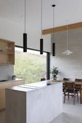The kitchen island responds to the concrete walls and floor, while black pendant lights punctuate the otherwise light palette.