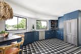 The black and white floor tiles in the bar area are complemented by the ebony Marvin Essential window frames and blue cabinetry that celebrates the couple’s love of midcentury design. Bamboo bar chairs and a feathered pendant light add a touch of playfulness.