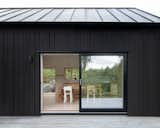 The cottage is wrapped in dark timber cladding that allows it to blend into the landscape, while the interior features white and natural timber finishes, making the most of the abundance of natural light to create a bright space.