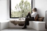 Designer Jules Moore sits in a window seat with her French bulldog, Sake. A New Zealand sheepskin rug and woven pillows from Turkey add a sense of warmth and comfort to the ledge, while the bronze casing of the Marvin Ultimate Awning Narrow Frame window captures the view like a painting.  Photo 6 of 14 in A Dilapidated Pueblo-Style House in Santa Fe Gets a Modern Makeover