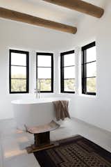 A freestanding bath is surrounded by a quartet of windows that invite sweeping views into the bathroom to create a relaxing oasis. Crafted touches, such as the carved timber stool and ornate rug, add texture to the space.
