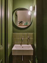 The upstairs bathroom was renovated to embrace the design language of the renovated kitchen, with green kit kat tiles behind the basin and a round mirror that echoes the skylights and rounded forms of the new scheme.