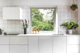 The white tiles used for the backsplash echo the boxy extractor fan and the under-counter cabinetry, creating a dynamic grid-like pattern.