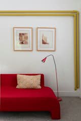The bright yellow heating pipes are playfully contrasted with a bold red sofa and matching lamp.