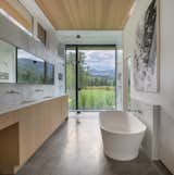 The primary en suite features a soaking tub and shower facing a floor-to-ceiling window that creates an illusion of being outdoors. The timber joinery echoes the materiality of the cabinetry in the kitchen.