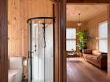 A curved glass shower enclosure and matte black fixtures give the bathroom a clean, modern finish—while the timber wall lining continues uninterrupted, echoing the simplicity and palette of the rest of the home.