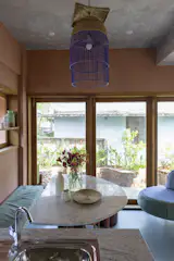 The pendant above the dining area is crafted from upcycled bird cages, painted blue to echo the color of the donated floor tiles used throughout the ground floor. The glass doors can be fully opened, extending the living area outside.