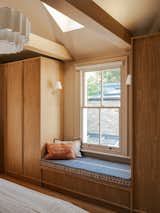 Along the side wall, oak wardrobes and a deep bench seat frame the window. Leila made many of the soft furnishings in the home herself—including the brightly patterned bench cushion.