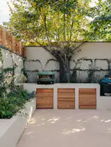 A low wall morphs from a bench seat to a planter to an outdoor kitchen with storage concealed behind timber doors that echo the interior joinery.