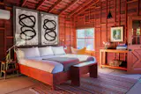 Guest rooms feature the property’s signature russet wood-clad walls adorned with abstract art, exposed beam ceilings, and concrete floors. The beds are topped with Swiss Army blankets.