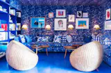 The blue theme continues into the communal lounge, which features a salon-style art wall and oversized wicker chairs. The collection includes work by David Hockney and Roy Lichtenstein.