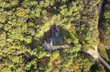 The L-shaped plan and detached garage sit within a clearing on the family’s two-acre wooded lot on Raynes Neck, a peninsula located about half a mile from the ocean. The cedar exterior of the home, Gendai Linseed Black yakisugi by Nakamoto Forestry, all but disappears into the surrounding forest.