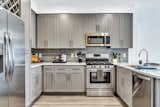 Gourmet kitchens boast white quartz counters, gray shaker cabinets with modern chrome hardware, stainless-steel appliances, a wine rack, and a full-height tiles backsplash.