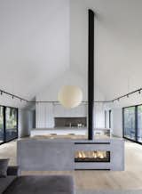 A central fireplace, designed as a minimal, gray block and visible from both sides, subtly separates the living and dining zones. 