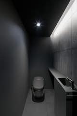 A bathroom tucked beneath the stairway has a cavernous quality. Everything—down to the toilet and Hansgrohe AXOR faucets—has the same charcoal shade. 