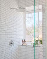 Economical white subway tiles in a classic running bond pattern in the primary bathroom give subtle visual interest to the restrained palette. The deep window creates a sense of privacy and is sill-capped with white quartz. 