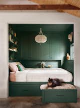 Bedroom, Shelves, Bed, Storage, Bookcase, Pendant Lighting, and Concrete Floor A wash of dark green paint introduces old-world drama to the sleeping nook. (The color is Billiard Green from Sherwin Williams.) The crochet pendant is from World Market, and the brass bull was an eBay find. The couple’s dog, Waylon, lounges in the pull-out dog bed drawer.