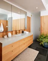In the primary bath, a cedar wall panel complements the oak vanity with adjusted concrete sink and counter. The floors are slate tiles according to CLO.