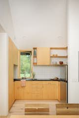 The food prep area sits adjacent to a small dining area in the middle structure of the three. Black Richlite countertops complement a white tile backsplash and maple cabinetry. The induction cooktop is from Bosch and the faucet is Grohe.