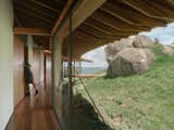 The home's corridor is framed by window walls that look out to the grassy hillside and a collection of boulders.