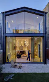 The new steel-and-glass rear facade expands views and daylight for the ground floor living areas and the primary bedroom above. The sliding glass doors are by Otiima Windows.
