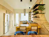 The kitchen features a marigold yellow zellige tile-clad island, the color of which was inspired by yellow desert flowers spotted during a rammed earth workshop in Arizona. The bar chairs are vintage Jeanneret.