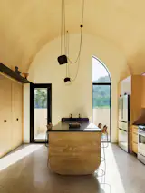 The ADU's compact kitchen features an eat-in island with a double sink that can be accessed from either side. Rammed earth is used on the end of the island. The pendant light is by FLOS.
