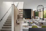 The living room opens to views of the exterior patio. The fireplace is clad in Italian marble with a built-in board-formed concrete bench. The casework is custom rift-sawn white oak, and the pendant over the dining table is by Foscarini.