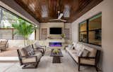 The covered lounge and entertainment area adjacent to the home includes a seating area, hearth and tv.  The soaring wood veneer ceiling is in contrast to the Travertine tile floor surfaces that ties in the color scheme of the entire indoor-outdoor space.  