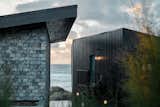 An external view through the main building and the annex out to sea. Black timber cladding on the contemporary new build pool house contrast the reclaimed roofing slates of the main house. 