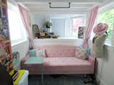 Natural light is available through a large bay window and two side windows. The pink couch has storage beneath and the C-shaped table can be slid under the couch to gain some extra floor space. Vintage details like the antique tray and the floral patterns give this living room a classic look that never goes out of style. 