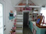 A staircase leads to the loft, while the kitchen features a long countertop with plenty of working space. The cabinets are treated with a custom color to brighten the space, and the ledge on the stove hood and loft provide plenty of space for a mini art gallery. Storage is disguised with colored baskets, and plenty of shelf space. 