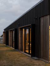 Glowing at dusk, the large glazed sliders are bordered with black steel hoods that aid in shading with interior lined natural wood that contrasts with the dark battened ply cladding. 