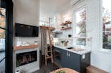 Gooseneck Tiny home with dark cabinets, brass hardware, white faucet, porcelain counters, and floating shelves by Tru Form Tiny