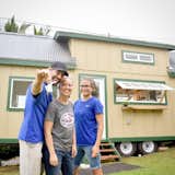 Happy owners! Some of my favorite people!! Love you guys. The beige and green exterior of this tiny home was painted to match a house on the same property as the unit is parked. You can see the mango wood exterior bar is on brackets that allow it to be folded down when not in use and for transport. You can also see a 1x4 propping open that awning window- don't mind that.