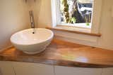Live edge mango wood vanity counter top cut in a triangular shape to fit in the corner of this tiny home bathroom. A vessel sink taking up less counter space. a window sill of the same wood as the vanity.