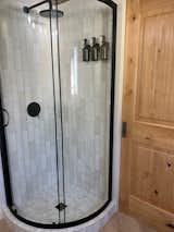 White tile shower with curved sliding glass shower door. corner shower- black accents