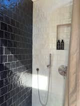The bathroom has natural edge Hawaiian mango wood slabs spanning the length of the bump-out: the vanity countertop and the shelf beneath. The entire bump-out-side wall is tiled floor to ceiling with a diamond print pattern. The shower follows the high contrast trend with one white wall and one black wall in matching square pearl finish. The warmth of the terra cotta floor adds earthy warmth that gives life to the wood. 3 wall lights hang down illuminating the vanity, though durning the day, you likely wont need it with the natural light shining in from two perfect angled long windows.  